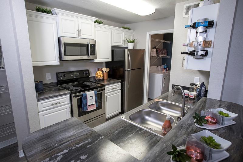 Signature Kitchens | Signature kitchens featuring black fusion countertops, stainless steel appliances, and wood-style flooring.