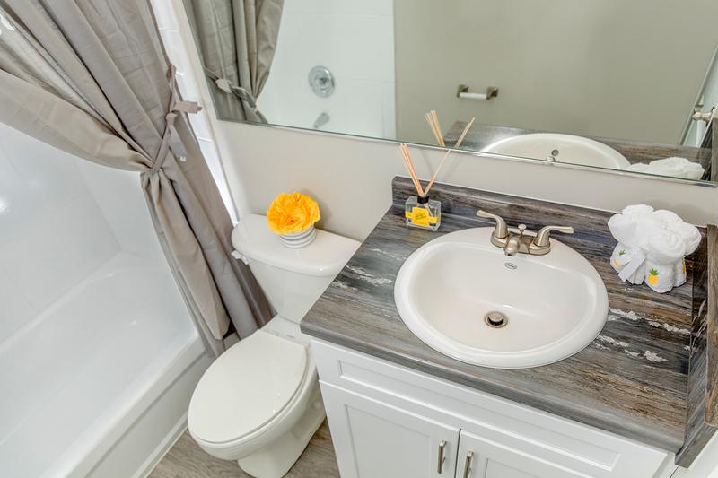 Renovated Bathrooms | Newly renovated bathrooms featuring black fusion countertops, large mirrors, and wood-style flooring.