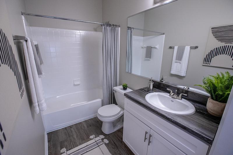 Bathroom | Renovated bathrooms feature black fusion countertops, wood-style flooring and large mirrors.