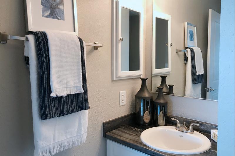 Bathroom | Updated bathrooms with black-fusion counter tops, large mirrors, and wood-style flooring.
