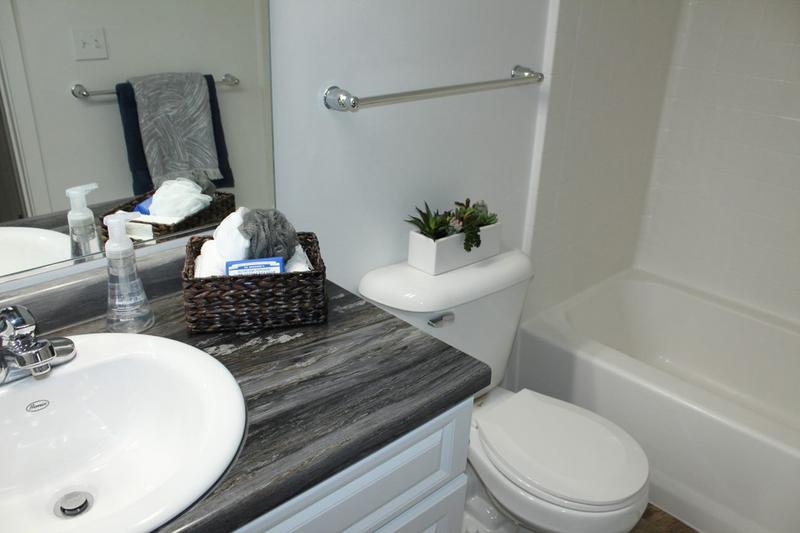 Renovated Bathrooms - In Select Homes | Updated bathrooms featuring black fusion countertops, wood-style flooring, and large mirrors.