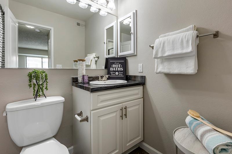 Bathroom | Newly remodeled bathrooms featuring granite-style counters, wood-style flooring, and a large mirror.