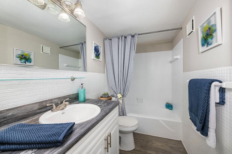 Bathroom | Updated bathrooms featuring marble-style countertops, wood-style flooring, and large mirrors. 