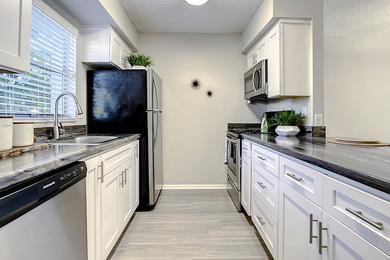 Galley-Style Kitchens | Select floor plans feature galley-style kitchens featuring black-fusion countertops, wood-style flooring, and stainless steel appliances.