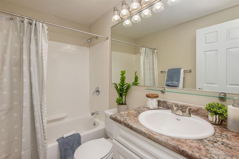 Bathroom | Newly renovated bathrooms featuring granite-style countertops, large mirrors, and wood-style flooring.