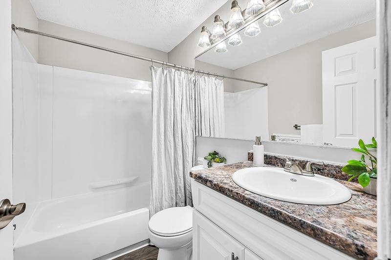 Bathroom | Newly renovated bathrooms featuring granite-style countertops, large mirrors, and wood-style flooring.