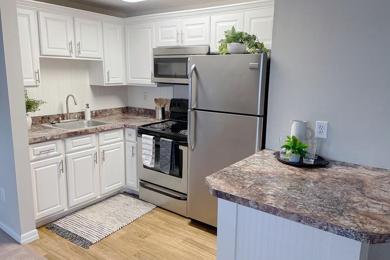 Modern Kitchens | The kitchen layout in The Willow floor plan features wood-style flooring, stainless steel appliances, and a mini breakfast bar.