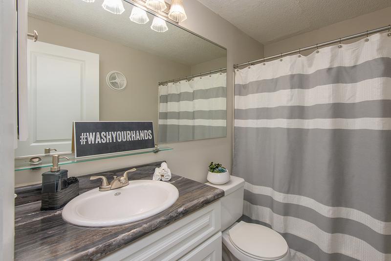 Bathroom | Newly remodeled bathrooms featuring wood-style flooring, black-fusion counter tops, and large mirrors.