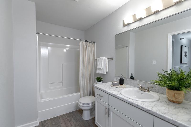 Bathroom | Updated bathrooms featuring white Carrera countertops, wood-style flooring, and large mirrors.
