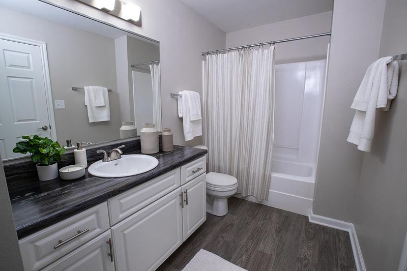 Bathroom | Modern bathrooms featuring wood-style flooring, black fusion countertops, and large mirrors. 