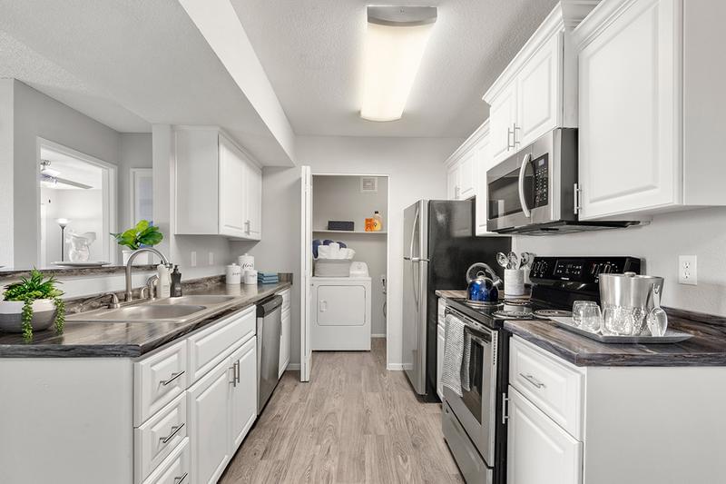 Open Kitchens with White Cabinetry | Beautiful open kitchens featuring black fusion counter-tops, white cabinetry, stainless steel appliances, breakfast bar and enclosed laundry room.