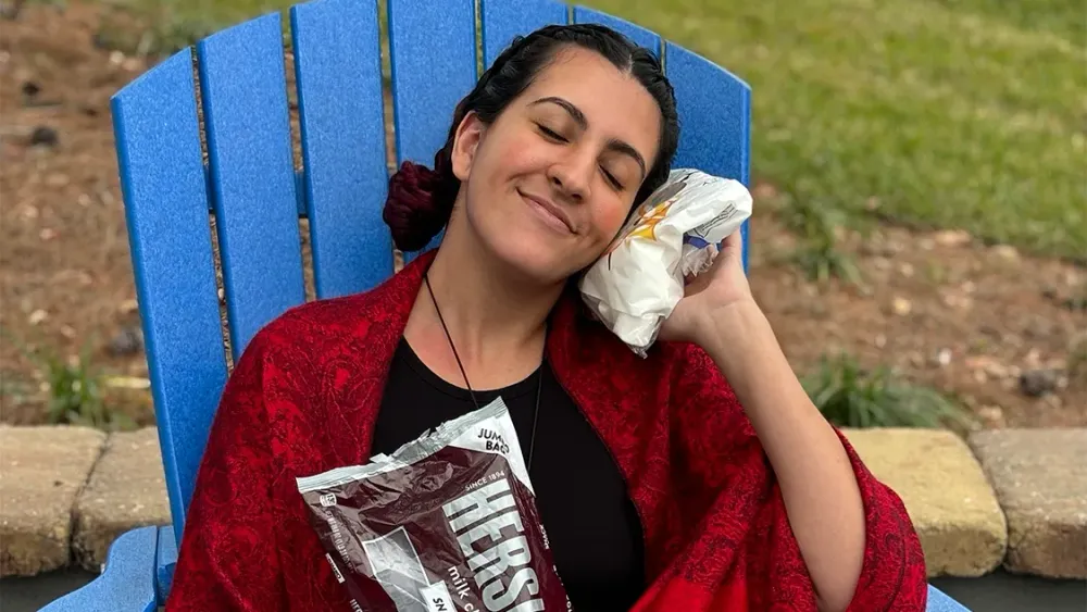 A woman holding a bag of marshmallows to her cheek in a blue chair, ready for s'mores.