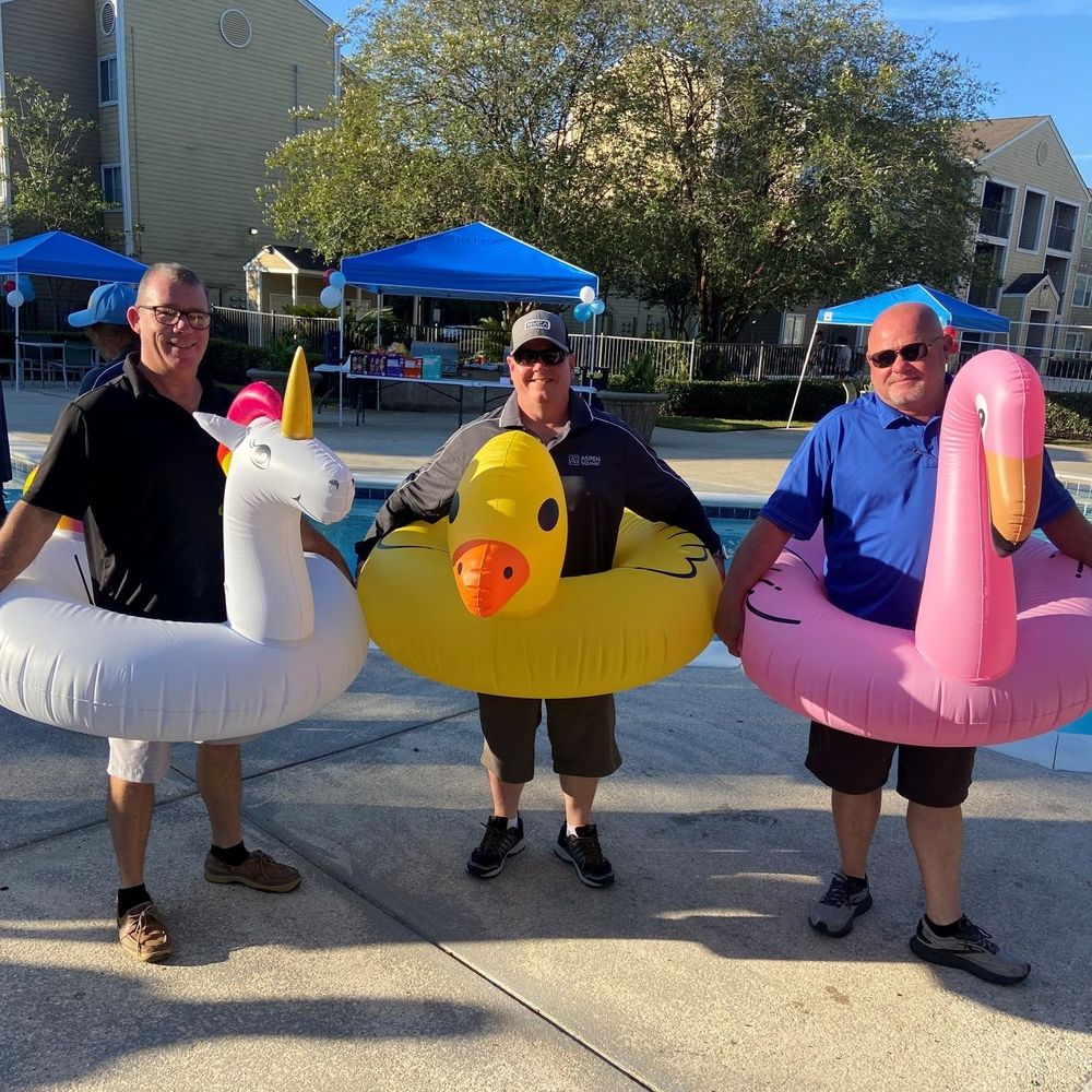 Three maintenance team members stand in a unicorn, flamingo, and duck pool floatie.