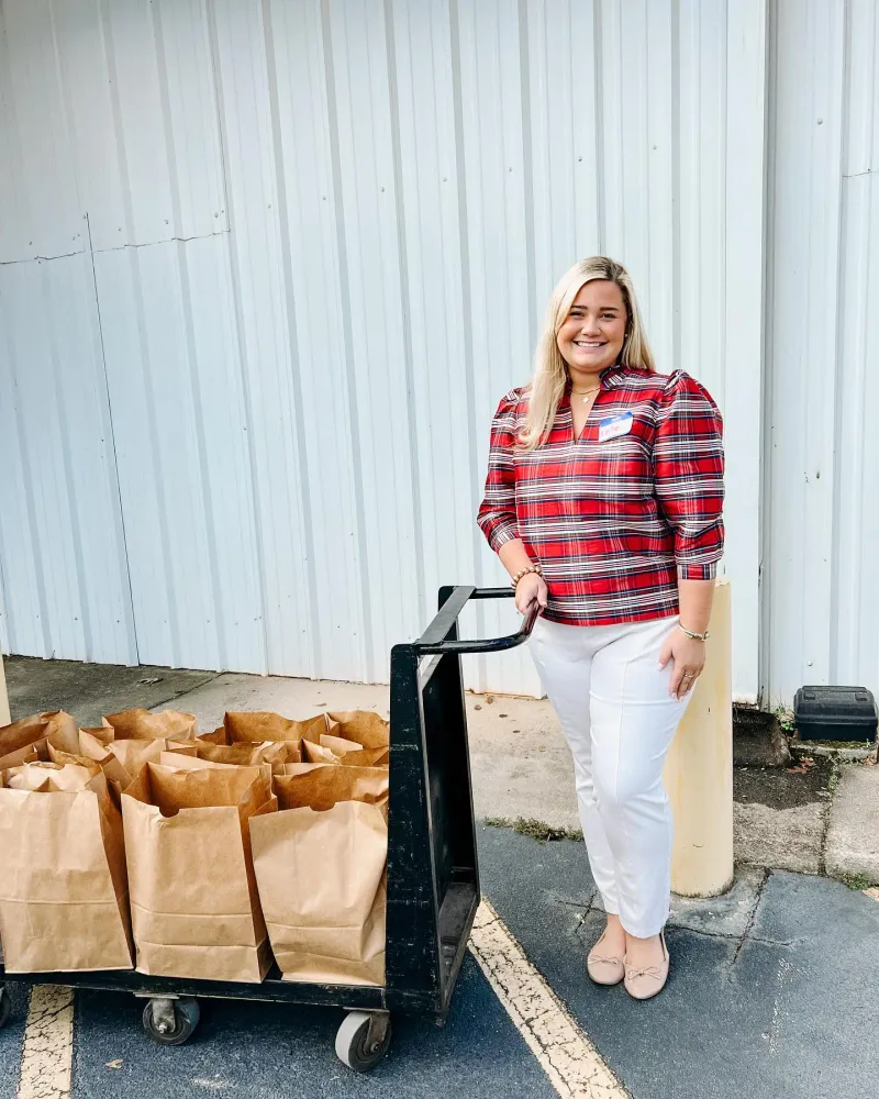 A woman in a plaid shirt stands with a cart of donated groceries. 