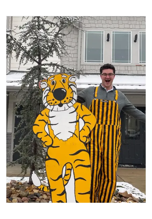 A man stands next to a cut out of the yellow Mizzou tiger mascot. 