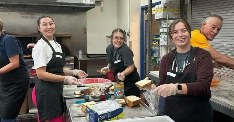Four people work in an industrial kitchen making sandwiches. 