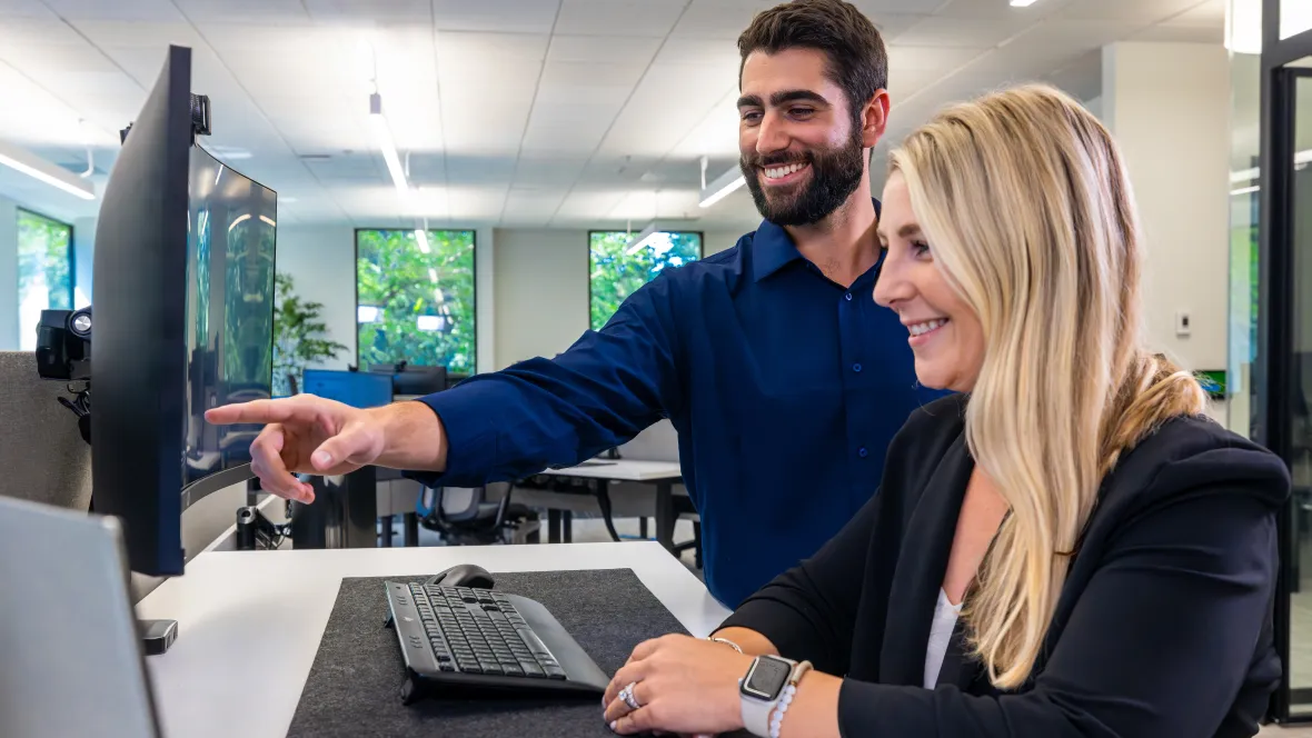 A man and woman looking over a computer together. Main is pointing at computer screen.