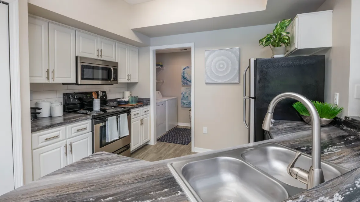Renovated kitchen with plentiful white cabinetry, black fusion countertops, stainless steel appliances, and a large double sink.