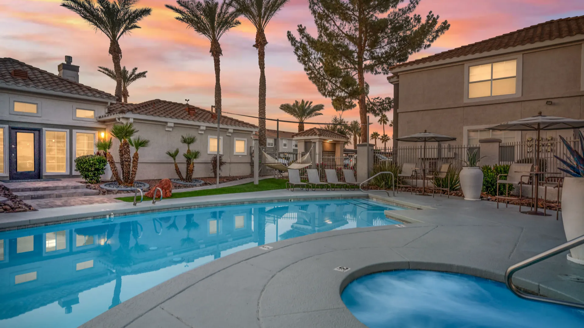 Resort-style pool and spa at Sedona Peaks during twilight, featuring lounge chairs, hammocks, and desert landscaping under a colorful sunset sky.