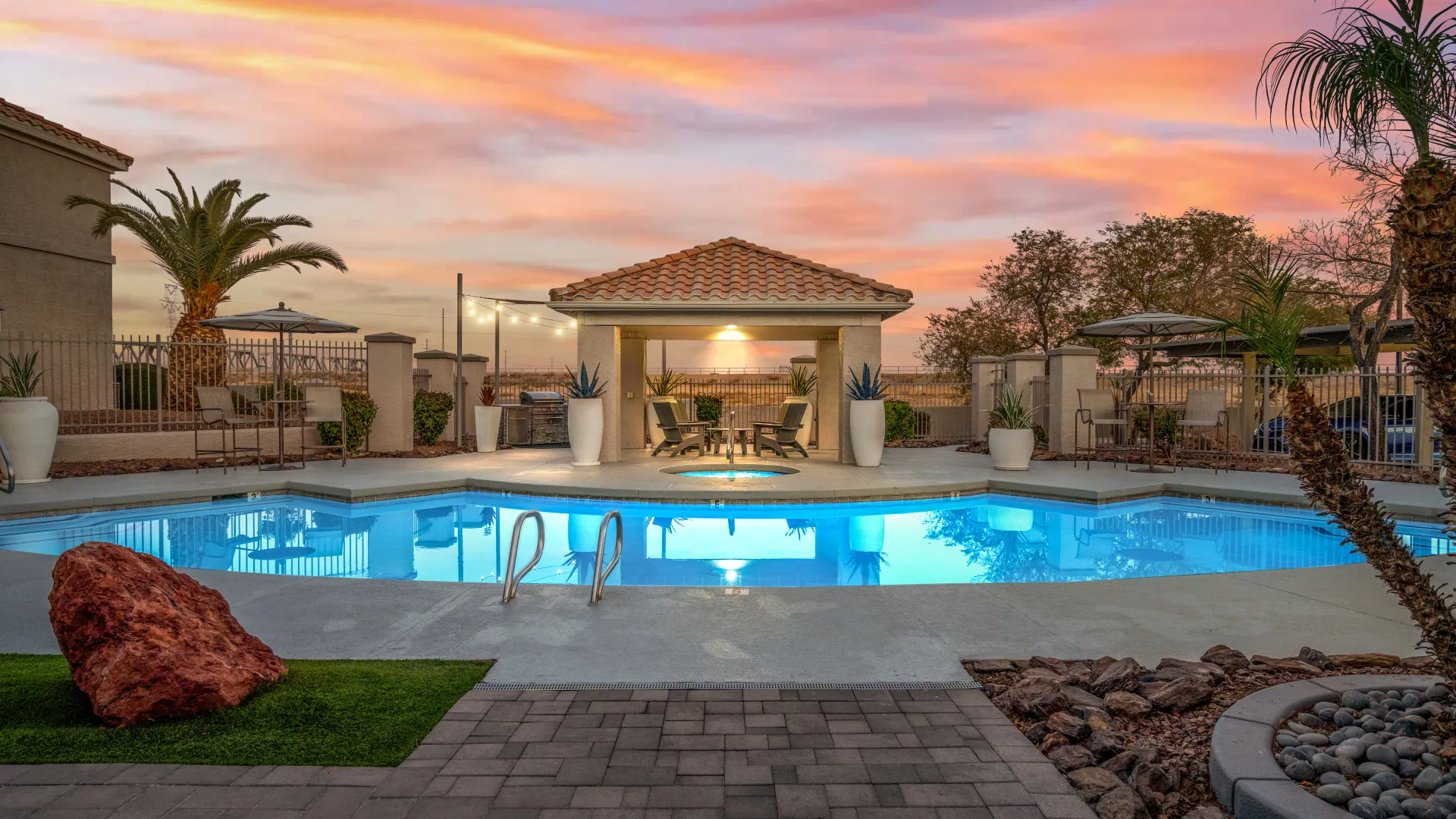 Resort-style pool at twilight with reflections of vibrant Arizona skies, cozy seating areas, shaded umbrellas, and a relaxing ambiance.