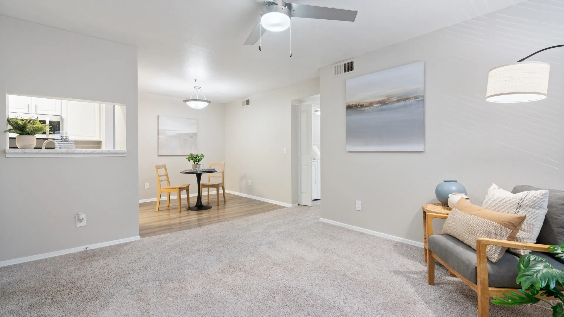 Spacious living room leading into a dining area, featuring a ceiling fan, soft carpeting, and bright walls.