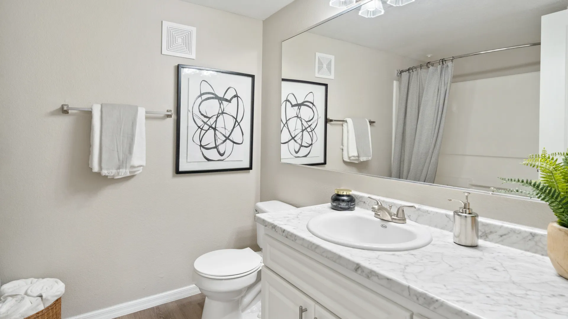 A bright and modern bathroom with a marble vanity, framed abstract artwork, soft towels, and a shower with a sleek gray curtain.