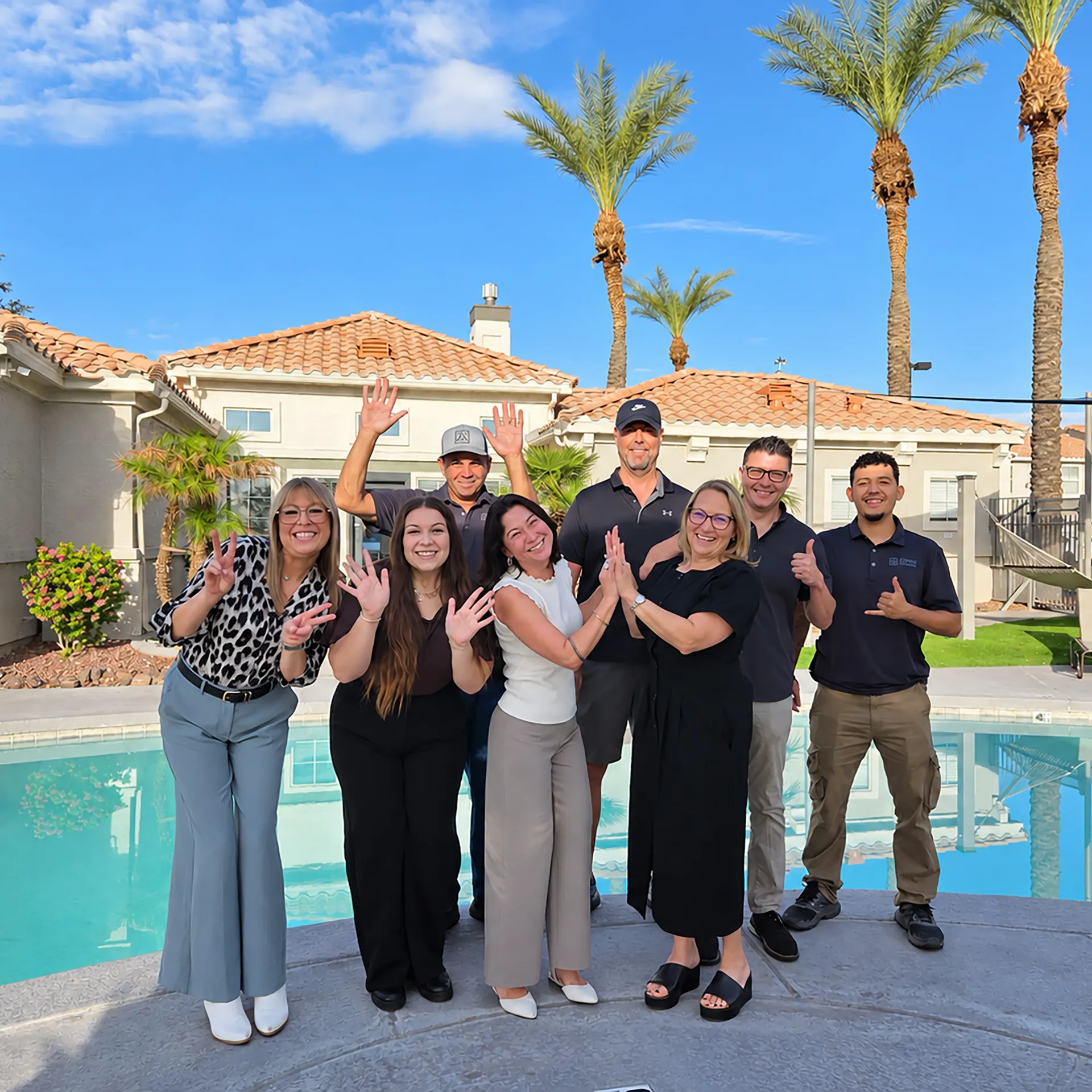 Group of eight Sedona Peaks team members standing together beside the community swimming pool on a sunny day.