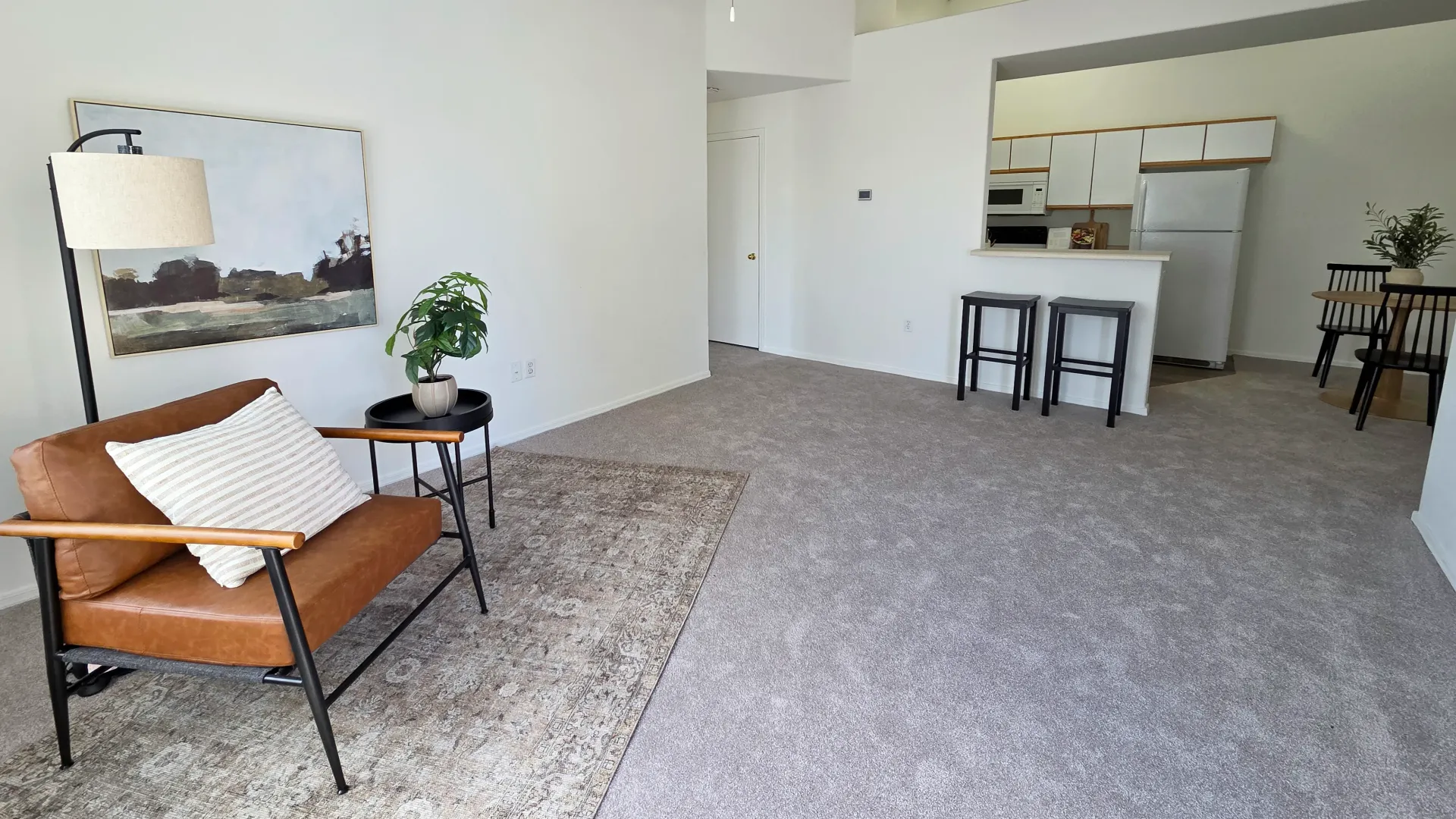 Bright, open living room featuring plush carpeting, high ceilings, and a breakfast bar connecting to the kitchen and dining area.