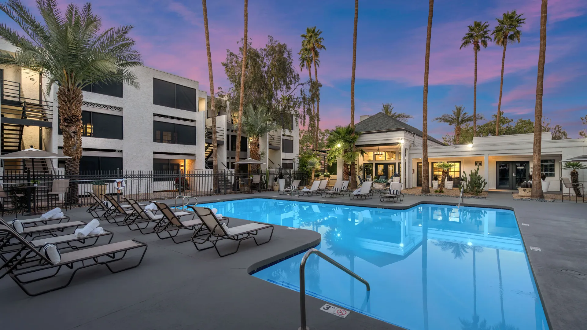 Twilight photo of pool surrounded by lounge chairs and palm trees