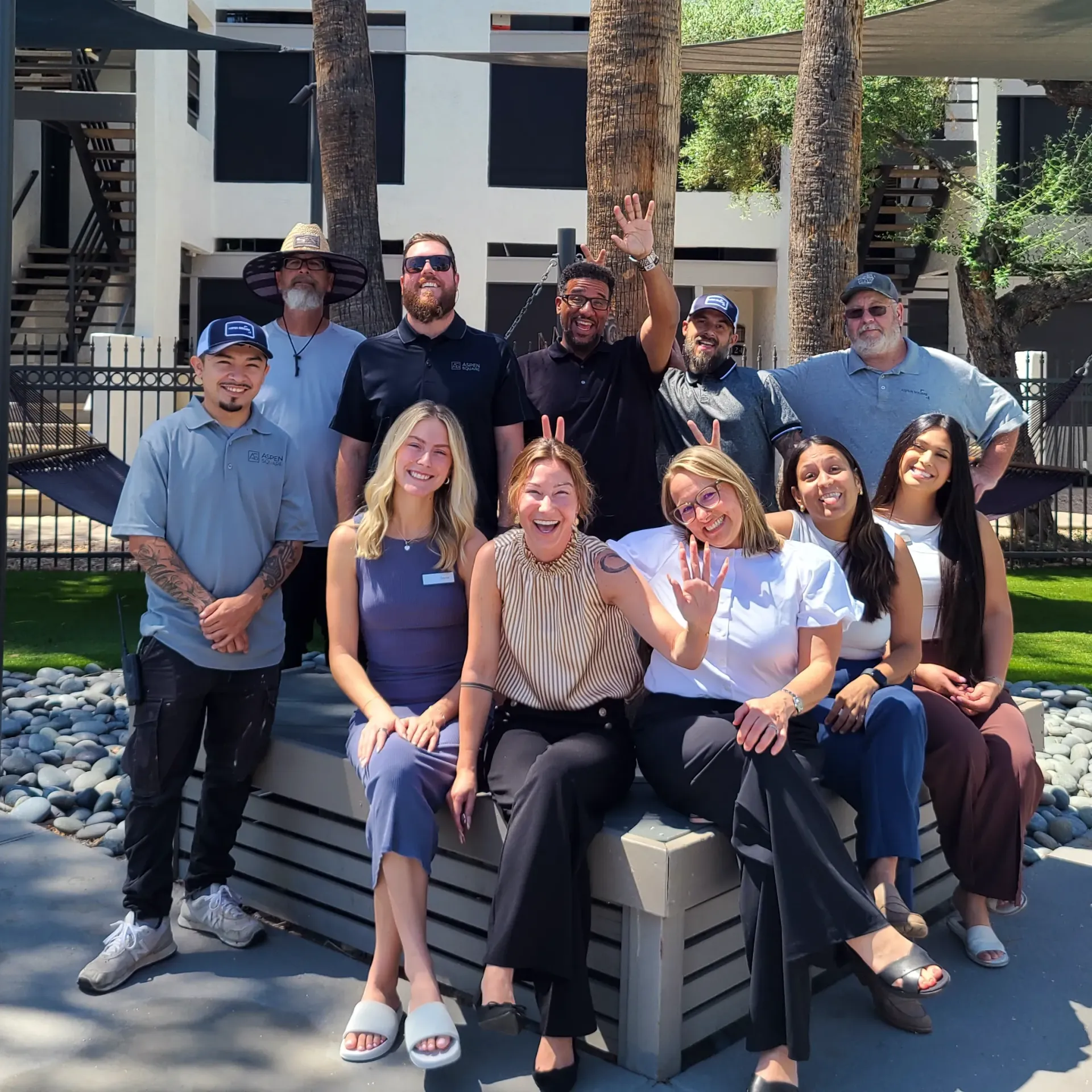 Beacon at 601 community team gathered outdoors in a landscaped courtyard with palm trees, hammocks, and apartment buildings.