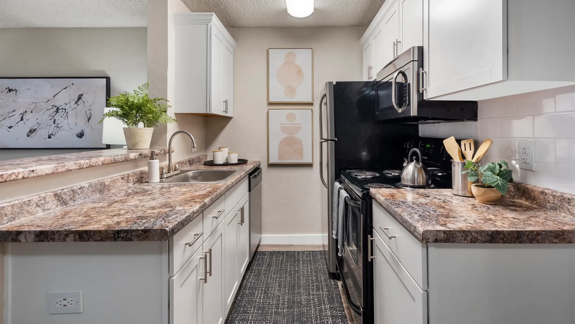 A galley-style kitchen with white cabinetry, granite-style countertops, and stainless-steel appliances 