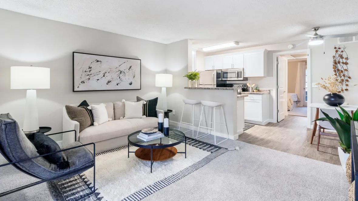 A chic living room with wood-style flooring flowing into a modern kitchen with a stylish breakfast bar.