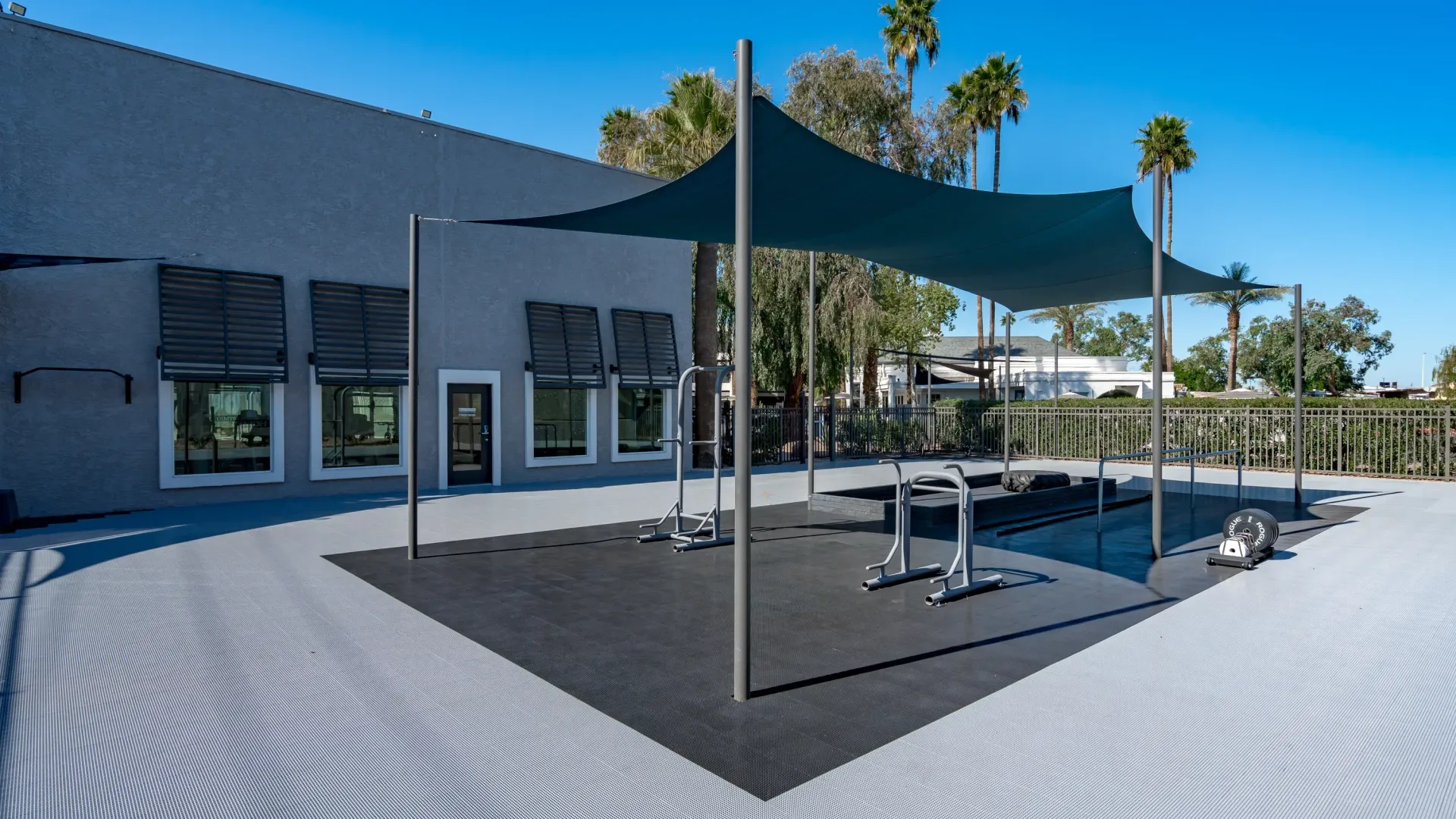 An outdoor fitness area with equipment and shade cloth. 