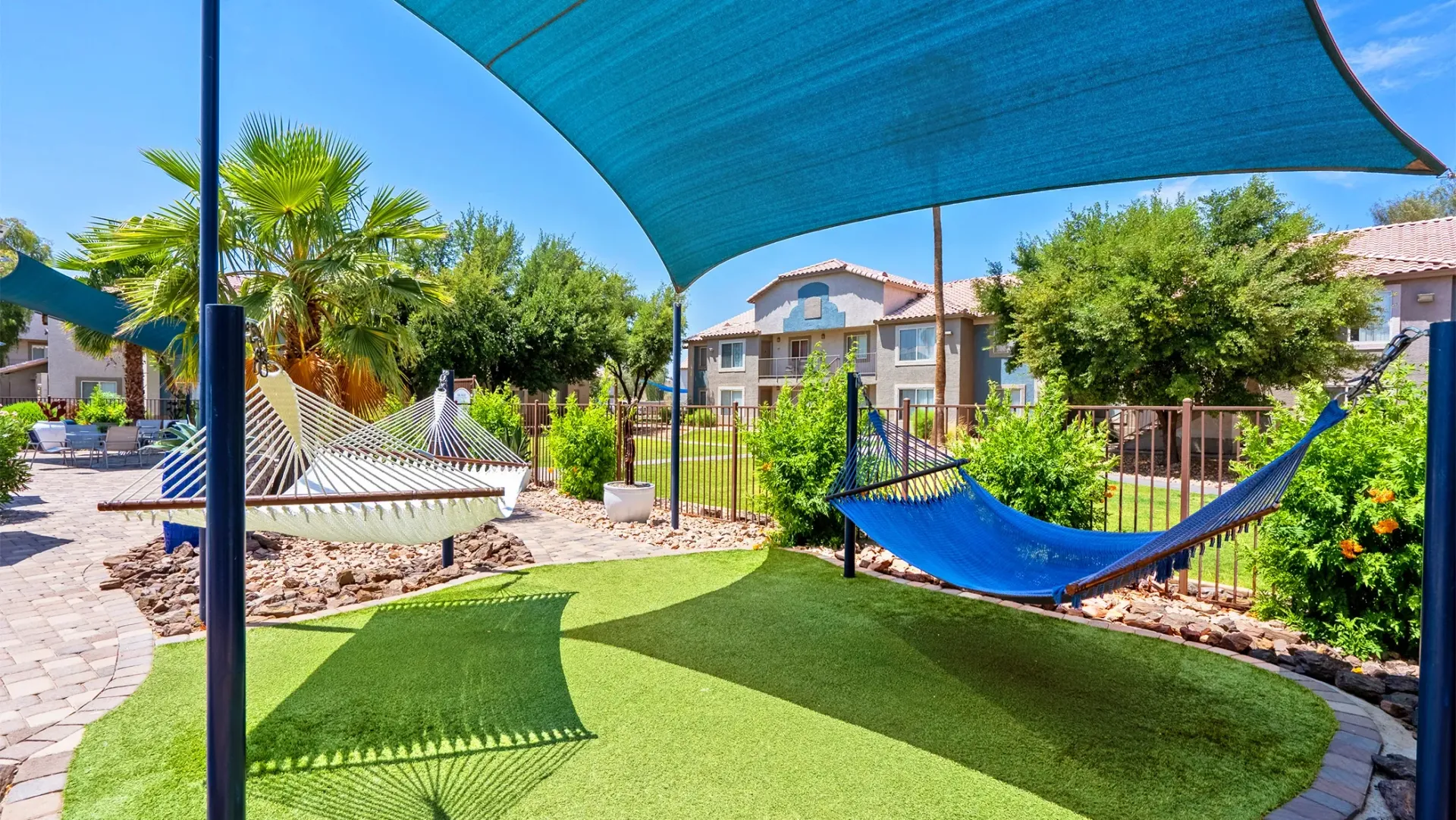 A patch of Astroturf with two hammocks hanging over, with a shade above