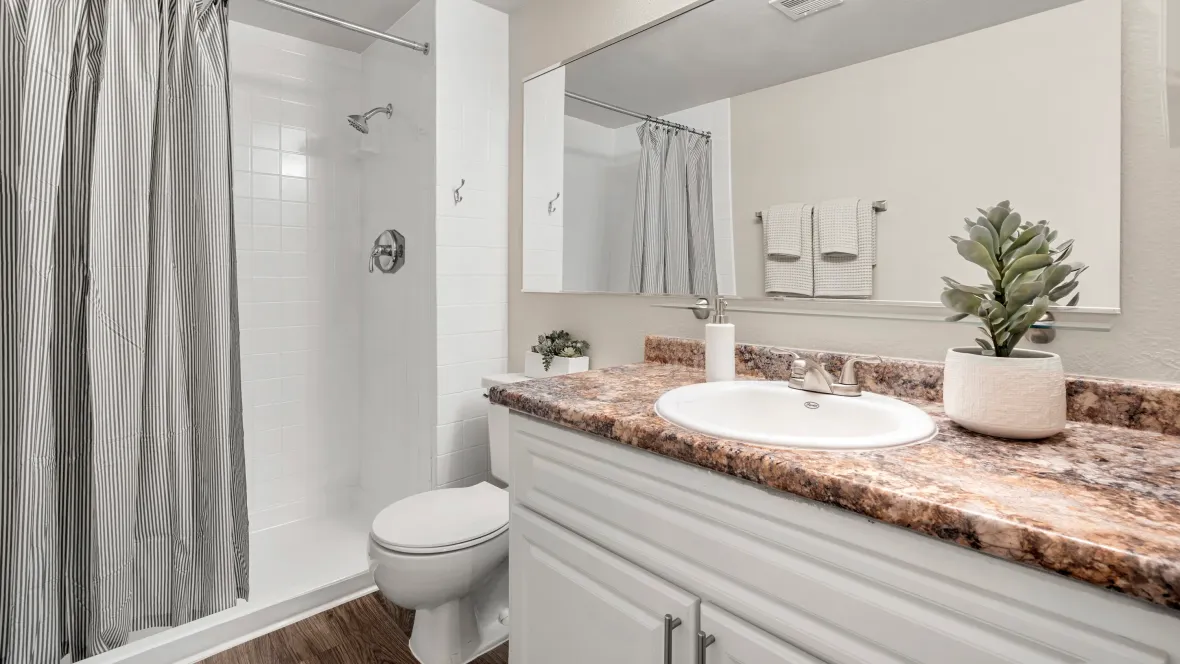 A luxurious master bathroom featuring a step-in shower with white tile surround, a spacious mirror for vibrant reflections, warm wood-style flooring, an oversized vanity for ample counterspace and storage, creating a serene escape.