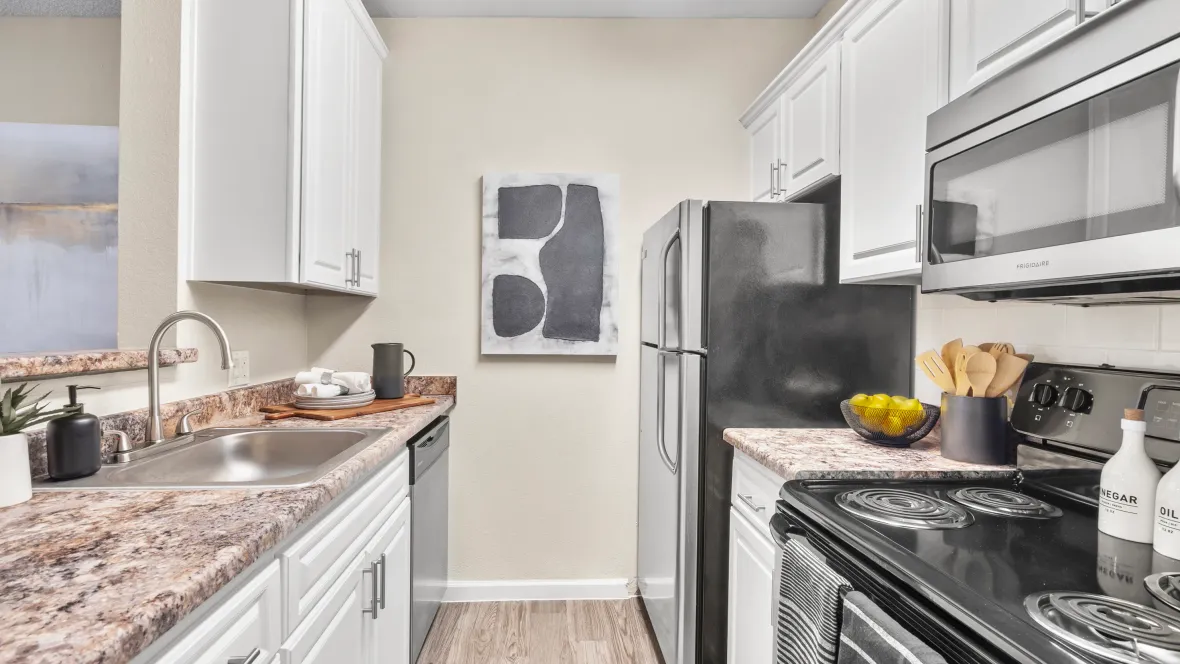 Modern, galley-style kitchen complimented by pristine white cabinetry and a suite of Frigidaire stainless-steel appliances, including a refrigerator, oven, microwave, and dishwasher.