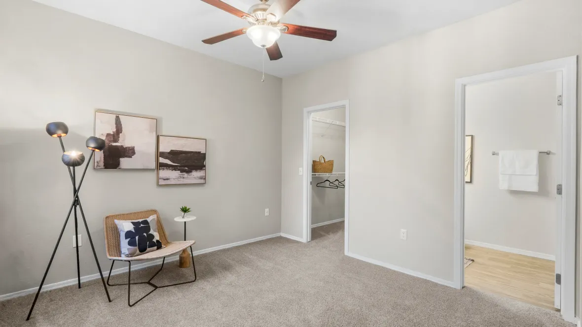 The well-lit bedroom boasts plush carpeting, a regal ceiling fan, and glimpses of the walk-in closet and master bath.