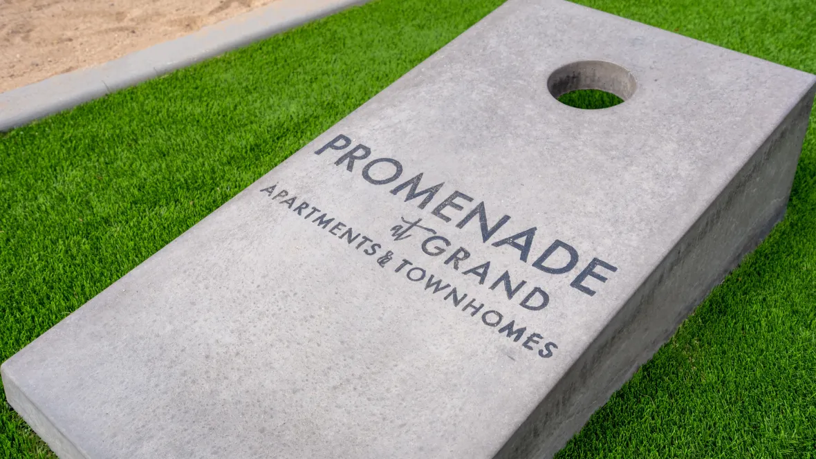 A close-up of our custom "Promenade at Grand Apartments & Townhomes" Cornhole board on the lush green court staged and ready for play.
