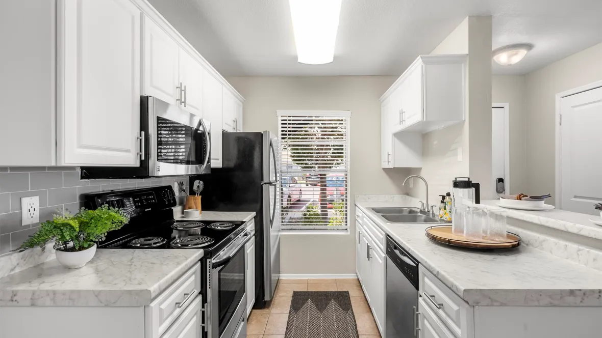 Elegant galley-style kitchen with white cabinetry, tan tiled flooring, and gleaming stainless-steel appliances.