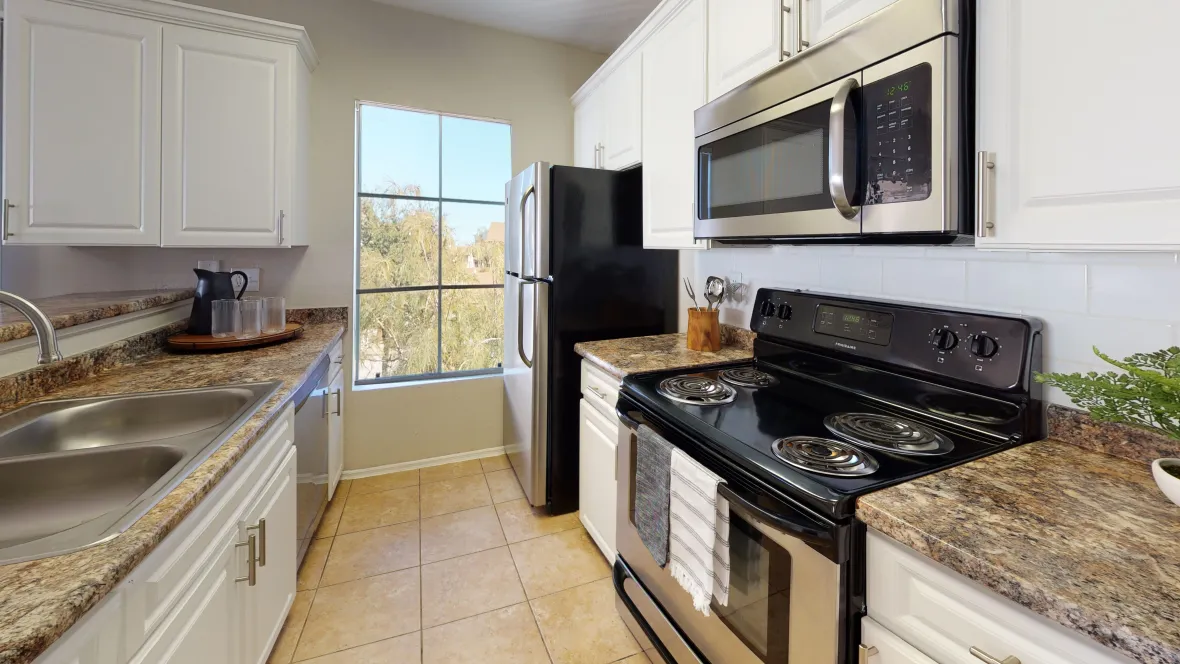 A galley-style kitchen with refined detailing including granite-like countertops, a white tile backsplash, a picture window as well as a full appliance package, including dishwasher.