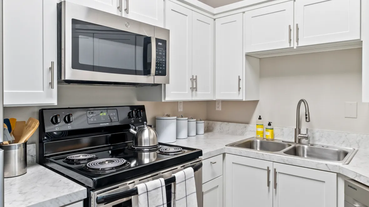 An exquisite corner of the superbly upgraded kitchen, showcasing the stove, microwave, double sink, dishwasher, and the radiant charm of white cabinets and countertops.