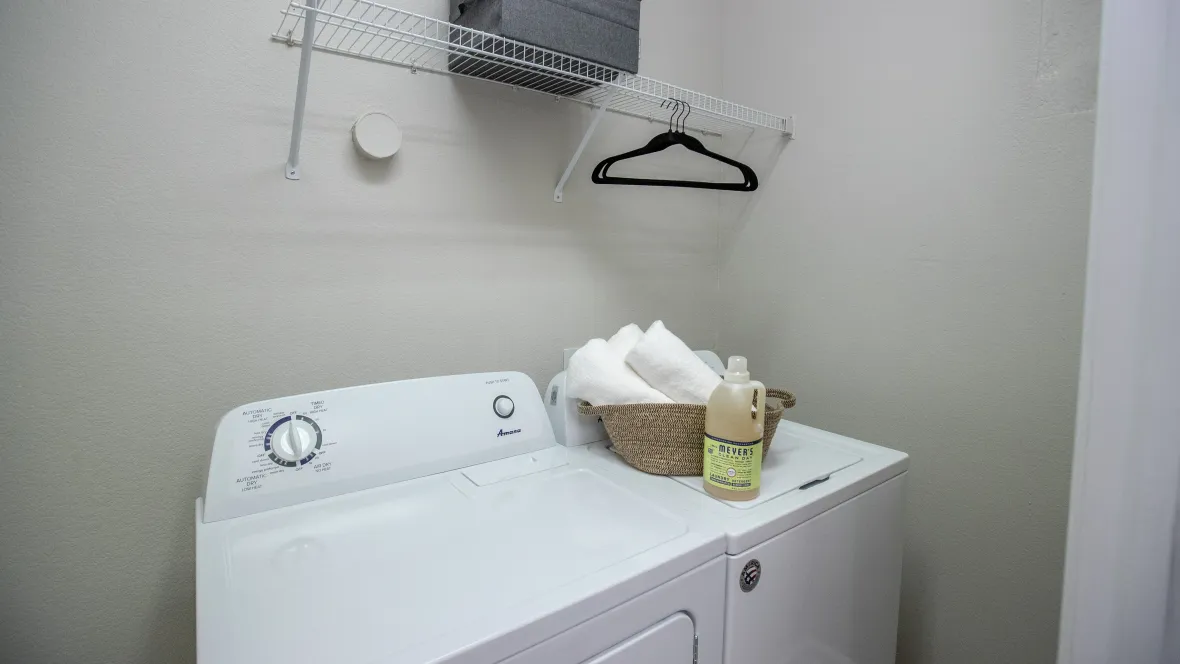 A spacious laundry area featuring a washer and dryer, accompanied by generous overhead shelving for neatly storing your supplies.