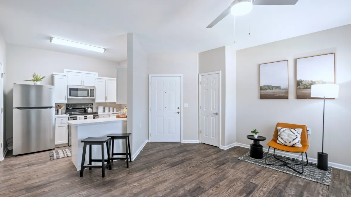 A living area exuding elegance, enhanced by a vibrant industrial ceiling fan and elegant wood-like flooring featuring a breakfast bar allowing open conversations across kitchen and living spaces.