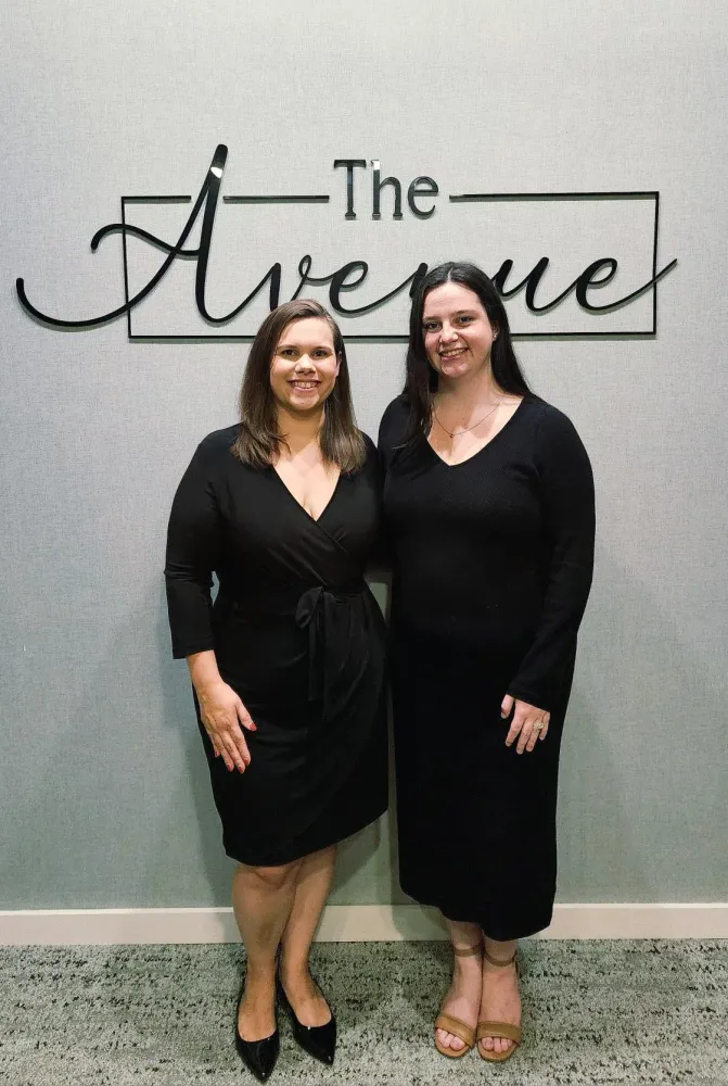 Leasing professionals from The Avenue Apartments in Cabot, AR posing inside the leasing office with The Avenue logo behind them.