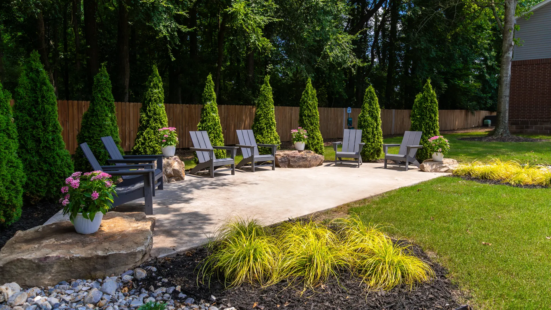 An outdoor seating area with Adirondack chairs surrounded by lush greenery and potted plants.