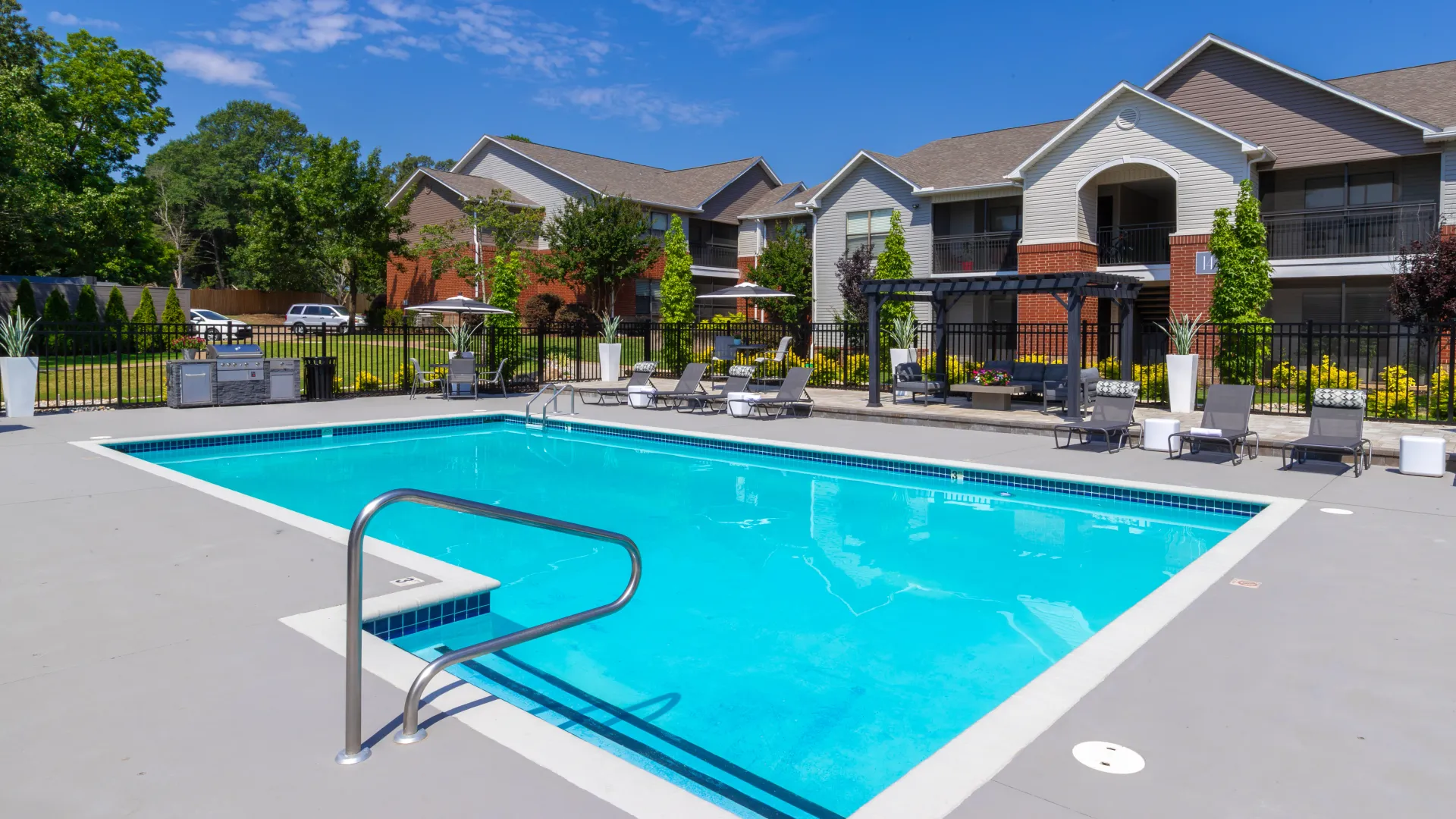 Outdoor swimming pool area featuring loungers, a BBQ area, and surrounding apartment buildings.