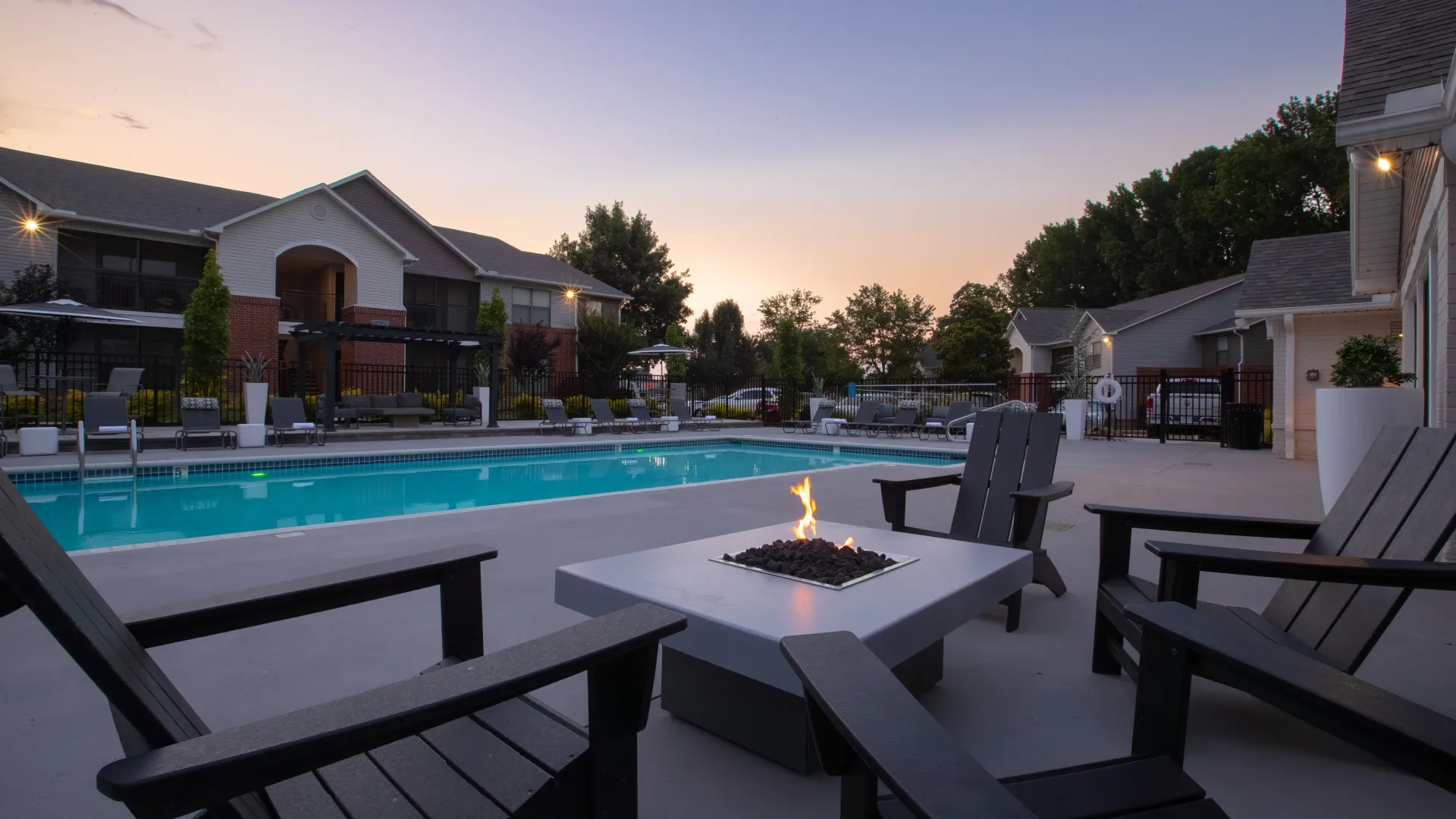 Pool area at sunset with a lit fire pit and Adirondack chairs.