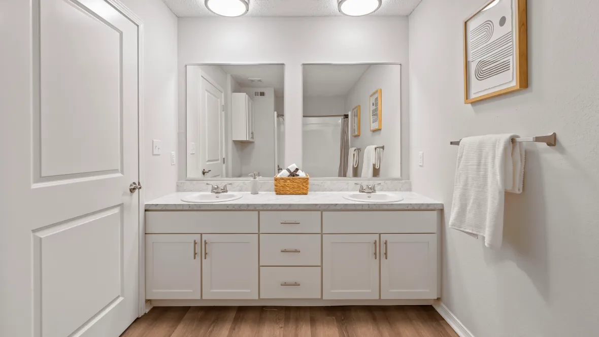 Two sinks with separate mirrors, plenty of storage, and warm wood-style flooring.