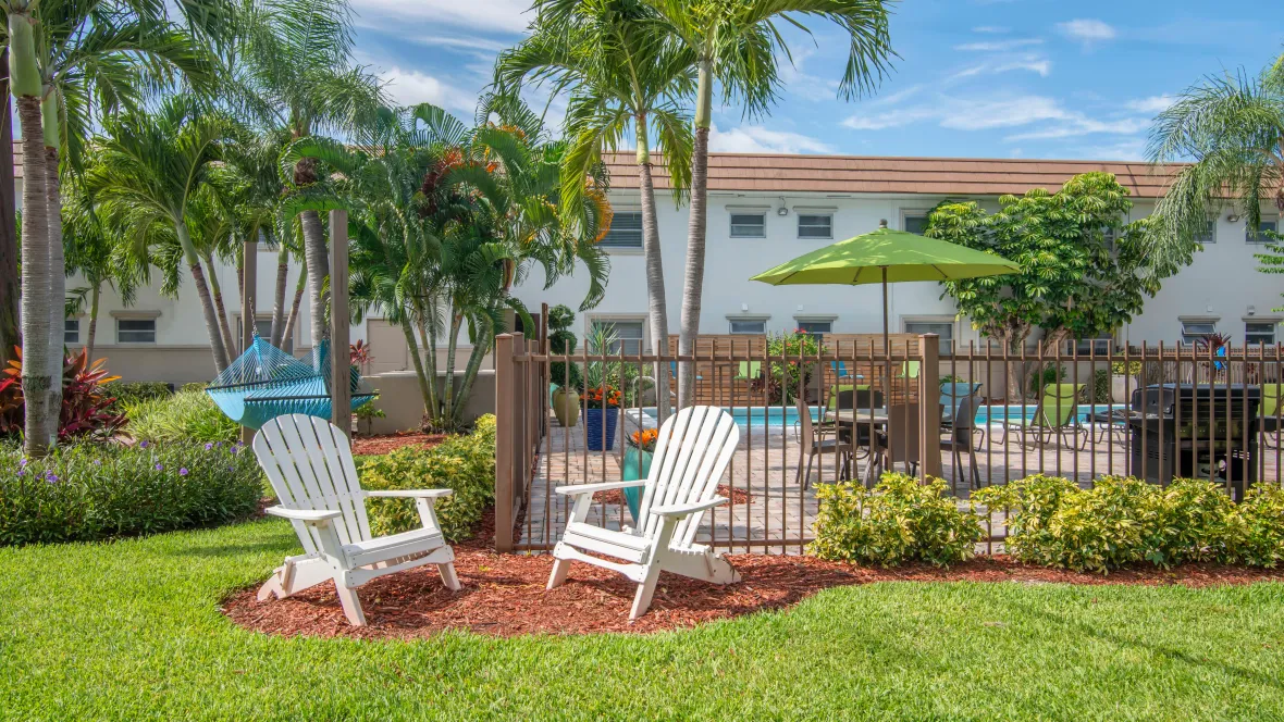 A cozy Adirondack seating area outside the pool gate, complete with a hammock and lush palm trees in the backdrop.