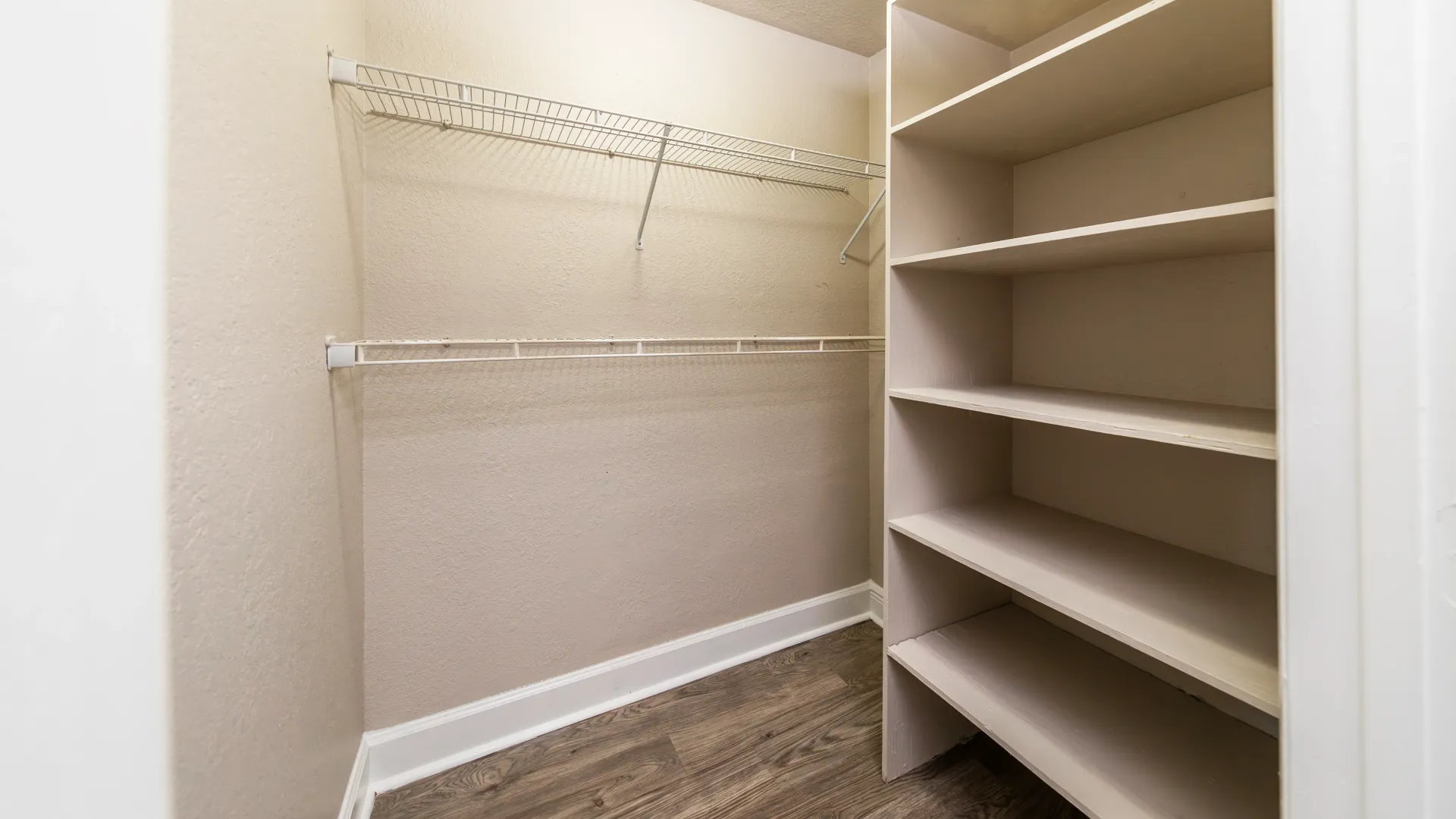 An expansive bedroom closet with two rows of open wire shelving, providing abundant storage space, and an integrated wooden shelf for organizing shoes and accessories.